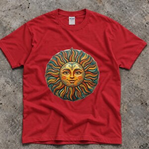 Può includere: Una t-shirt rossa a maniche corte con una grafica centrale raffigurante un sole stilizzato con un volto umano. Il design del sole incorpora motivi complessi in tonalità arancione, giallo, verde acqua e oro, con raggi ondulati che si irradiano.