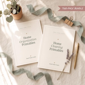 Könnte beinhalten: Zwei cremefarbene Papierhefte mit den Titeln Home Organization Printables und Home Cleaning Printables von Small Home Studio. Die Artikel sind mit einem goldenen Stift, einer Holzklammer, einem Lavendelzweig und einem salbeigrünen Band arrangiert.