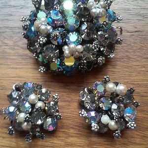 May include: A vintage brooch and earrings set featuring a cluster of iridescent blue and clear rhinestones and faux pearls in a silver tone setting.