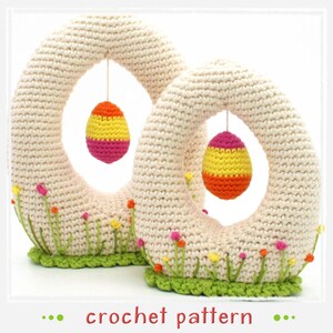 May include: Two crocheted Easter egg arches with hanging crocheted eggs. The arches are cream colored with green grass and pink, yellow, and orange flowers at the base. The eggs are pink, yellow, and orange.