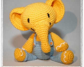 May include: A yellow crocheted elephant toy wearing light blue overalls with orange buttons. The elephant has large ears, a trunk, and white wavy stitching on its feet. The text "crochet pattern" is printed in green at the bottom of the image.