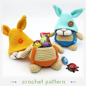May include: Crochet pattern for a bunny-shaped Easter basket with a yellow, blue, and beige color scheme. The basket is filled with colorful chocolate eggs and candy. A ladybug is sitting on the table next to the basket.