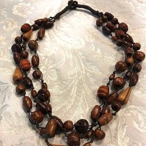 May include: A multi-strand necklace made of brown and light brown wooden beads. The necklace is made of several strands of beads that are knotted together.