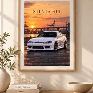 Könnte beinhalten: Ein gerahmter Kunstdruck, der ein weißes Silvia S15 Auto bei Sonnenuntergang in einem Hafen zeigt. Der Text lautet SILVIA S15 JAPANESE STREET ICON und JDM SERIES 1999. Der Druck befindet sich in einem hellen Holzrahmen mit einem weißen Passepartout.