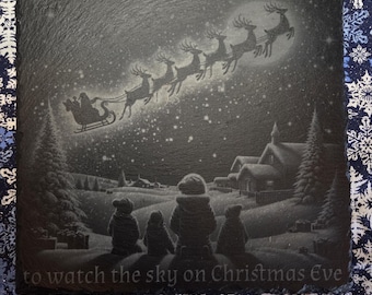 Könnte beinhalten: Eine quadratische schwarze Schieferplatte mit einer Gravur einer winterlichen Szene, in der vier Kinder den Weihnachtsmann im Rentierschlitten betrachten. Der Text lautet: May you never be to old to watch the sky on Christmas Eve.