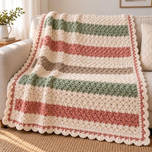 Pode incluir: Uma manta de crochê retangular com listras horizontais em creme, verde sálvia, rosa antigo e bege. A manta é feita com um padrão de ponto texturizado e finalizada com uma borda festonada em fio de cor creme e rosa antigo.