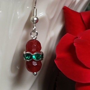May include: Red and green dangle earrings with silver hooks. The earrings feature two red faceted beads with a green rhinestone band around the centre.