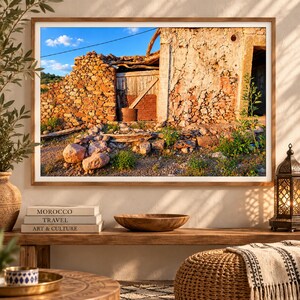 Peut inclure: Une photographie de paysage encadrée représentant un bâtiment en pierre usé avec une porte en bois et un mur en pierre rustique sous un ciel bleu vif. La scène est éclairée par la lumière dorée du soleil, soulignant la maçonnerie texturée.