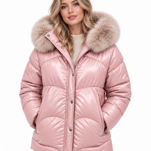 Puede incluir: Una chaqueta acolchada de color rosa metálico brillante con cuello alto y una capucha grande ribeteada con piel sintética beige. La prenda cuenta con un cierre frontal de cremallera oculto por una solapa con botones a presión y mangas.