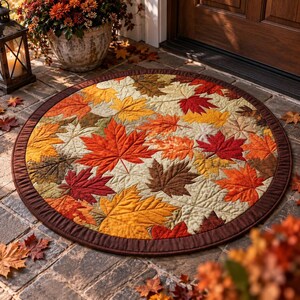 May include: A round quilted mat featuring a vibrant pattern of autumn leaves in shades of red, orange, yellow, and brown. The mat has a solid dark brown fabric border and intricate stitching that outlines the shape of each individual leaf.