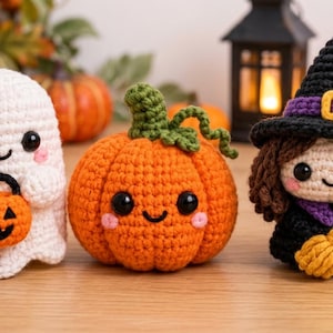 May include: Three handmade crochet amigurumi figures: a white ghost holding an orange jack-o'-lantern bucket, a round orange pumpkin with a green stem, and a witch wearing a black hat with a purple band, holding a small yellow broomstick.