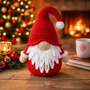 May include: A crocheted gnome figurine featuring a tall, pointed red hat with a white pom-pom at the tip, a round beige nose, and a long, textured white beard. The gnome has a round red body, beige hands, and white cuffs on its sleeves.