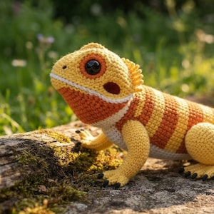 Op de afbeelding: Een gehaakt baardagaam speeltje met een geel en oranje gestreept lichaam, een witte buik en een groot zwart plastic oog. De hagedis heeft kleine zwarte klauwtjes aan de voeten en een textuur van garen met duidelijk zichtbare steken.