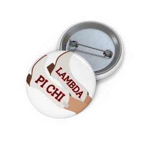 May include: A round pin-back button featuring a graphic of two white cowboy boots with brown accents. The text PI CHI and LAMBDA is printed in red with black outlines across the boots. The back of the button shows a silver metal pin mechanism.