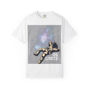 May include: A white short-sleeve t-shirt featuring a graphic of an astronaut floating in space against a grey nebula background. The text "NO LIMITS" is printed in white, and the vertical text "DARK NIGHTS BRIGHTER FUTURES" is visible.
