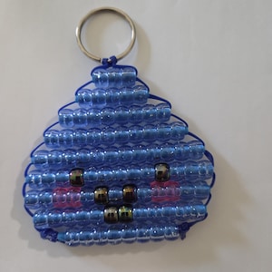 Könnte beinhalten: Ein Schlüsselanhänger aus blauen Kunststoffperlen, die in einer dreieckigen Form angeordnet sind, mit einem silbernen Metallring an der Spitze. Das Design zeigt Reihen aus transparenten blauen Perlen mit dunklen und rosa Perlen.
