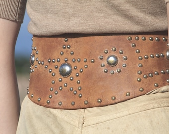 May include: A brown leather belt with silver studs and large round silver accents. The belt is decorated with a star pattern.