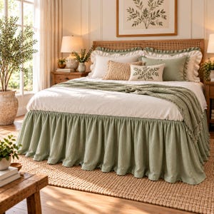 May include: A bed featuring a sage green ruffled bed skirt, a white duvet, and a sage green throw blanket. The bedding includes two white pillows, a sage green pillow, a textured tan pillow, and a small white pillow with a green leaf print.