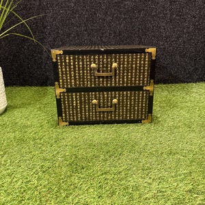 May include: A black rectangular storage chest with two drawers, featuring gold-toned metal corner brackets and U-shaped drawer pulls. The exterior surfaces are covered in black paper printed with dense columns of traditional Chinese characters.