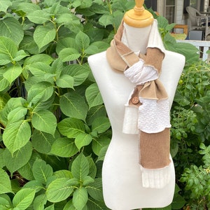 May include: A brown and white scarf with a button detail. The scarf is made of different fabrics and is layered to create a unique look.