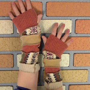 May include: Fingerless gloves in shades of rust, tan, and cream. The gloves feature a ribbed cuff and a patchwork design with patterned knit sections. The design includes a mix of textures and colors, creating a unique and cozy accessory.