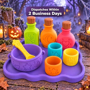 May include: A purple tray holding a purple cauldron with a yellow spoon, three bottles in lime green, orange, and pink with brown caps, and three small cups in teal, yellow, and orange, all featuring embossed celestial and floral designs.