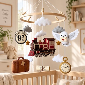 Könnte beinhalten: Ein Baby-Mobile mit einem Holzring und hängenden Filzelementen, darunter eine rot-braune Dampflokomotive, eine weiße Eule mit Briefumschlag, ein brauner Koffer, eine Uhr, ein Platform 9 3/4 Schild, ein Zugticket sowie weiße und graue Wolken.
