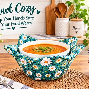 May include: A fabric bowl cozy featuring a teal background with a white and yellow daisy pattern, holding a white bowl filled with orange soup. The text "Bowl Cozy Keep Your Hands Safe & Your Food Warm" is visible in the upper left corner.