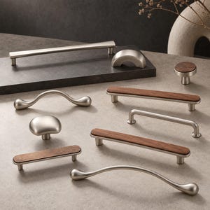 May include: A collection of cabinet hardware including brushed nickel metal pulls and knobs, some featuring dark wood inlays. The set includes curved handles, straight bar pulls with wood accents, and round knobs in various shapes and sizes.