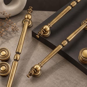 May include: A collection of antique brass hardware including two long, slender cabinet pulls with decorative spherical accents and two matching round cabinet knobs, all featuring a brushed metallic finish and circular mounting bases.
