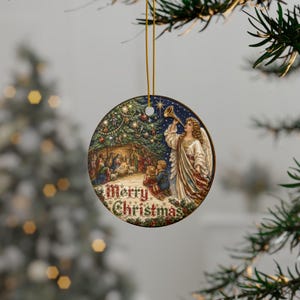 May include: A round ceramic Christmas ornament featuring a detailed illustration of a nativity scene under a decorated tree with an angel playing a trumpet. The text Merry Christmas is printed in red and green at the bottom of the circular ornament.