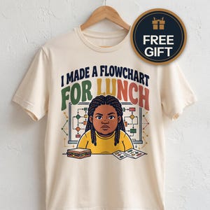 Könnte beinhalten: Ein cremefarbenes T-Shirt mit einer Grafik einer Person mit geflochtenem Haar, die an einem Tisch mit einem Sandwich und einem Flussdiagramm sitzt. Der Text I MADE A FLOWCHART FOR LUNCH steht in dunkelblauen, grünen und orangen Buchstaben.