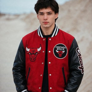 May include: A red and black varsity jacket featuring the Chicago Bulls logo on the chest and sleeve. The jacket has a red wool-like body, black leather-like sleeves, a striped ribbed collar and cuffs, and silver-toned snap button closures.