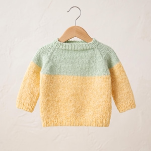 May include: A long-sleeve knit sweater featuring a color-blocked design with a light mint green upper section and a bright yellow lower section. The garment has a ribbed crew neckline, ribbed cuffs, and a ribbed hem, all crafted in a soft yarn.