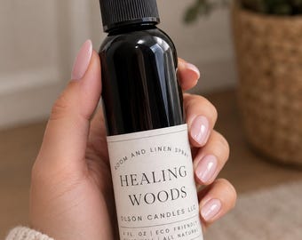 May include: A black plastic spray bottle with a clear cap and a white label. The label reads Room and Linen Spray, Healing Woods, Olson Candles LLC, 4 fl. oz, Eco Friendly, Shake Well, All Natural in black text on a white background.