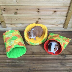 Peut inclure: Trois lits pour animaux de compagnie colorés pour petits animaux, tels que des cochons d'Inde ou des hamsters. Les lits sont faits de tissu avec un imprimé d'agrumes et ont une doublure douce et verte. Un lit est un lit rond et plat, et les deux autres sont des tunnels.