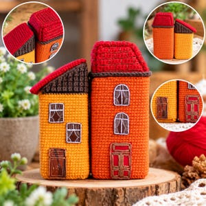 Pode incluir: Duas figuras de casas em crochê com telhados vermelhos e paredes texturizadas. A casa mais baixa é amarela com detalhes castanhos, enquanto a mais alta é laranja com detalhes vermelhos. Ambas possuem janelas e portas bordadas com costuras.
