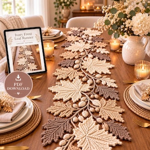 Pode incluir: Um caminho de mesa em crochê com um padrão repetitivo de folhas de bordo e bolotas em tons de creme, bege e castanho. Um tablet exibe o texto Ivory Frost Leaf Runner Crochet Pattern e PDF Download ao lado do caminho de mesa.