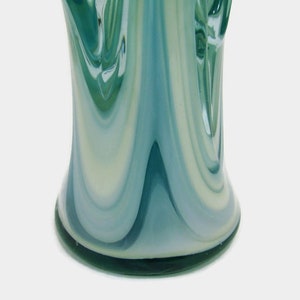 May include: A glass vase featuring a swirling pattern of teal, light blue, and white colors. The surface has a smooth, glossy finish with vertical, elongated streaks that create a fluid, marbled appearance throughout the cylindrical body.