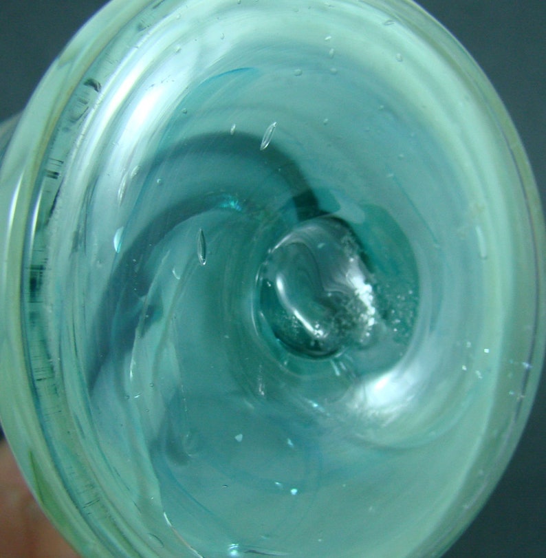 May include: A circular glass object featuring a swirling pattern of translucent light blue and white colors. The surface is smooth and clear, containing small trapped air bubbles throughout the material, with a central indentation.