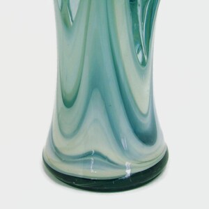 May include: A glass vase featuring a swirling pattern of translucent teal, light blue, and opaque white colors. The design consists of vertical, elongated streaks that blend together, creating a fluid, marbled appearance across the surface.