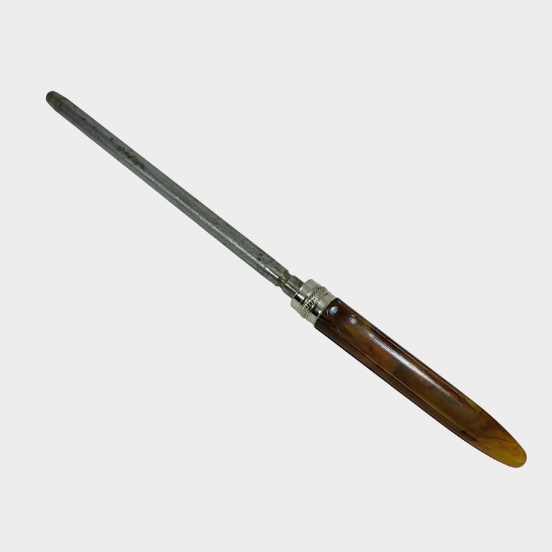 Puede incluir: Un afilador de cuchillos con un mango marr&oacute;n y una varilla de acero plateado. El mango tiene forma redondeada y est&aacute; hecho de un material marr&oacute;n oscuro. La varilla de acero es larga y delgada.