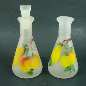 May include: Two frosted glass bottles with painted fruit designs. The bottles are clear glass with a frosted finish and feature hand-painted pears and apples in shades of yellow, orange, and green.