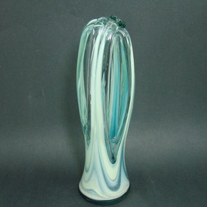 May include: A tall, slender glass vase featuring a swirling pattern of translucent teal, clear, and opaque white glass. The design incorporates elongated vertical loops that create an open, cage-like structure, tapering toward a solid, rounded base.