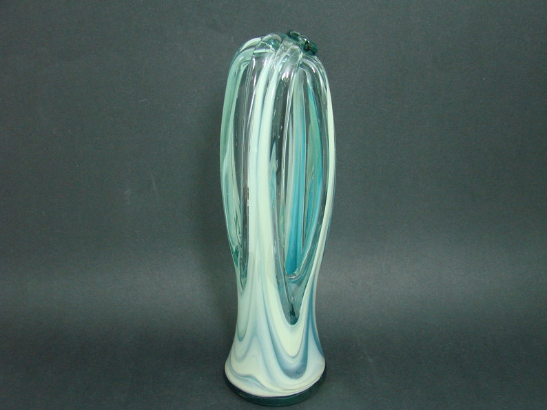 May include: A tall, slender glass vase featuring a swirling pattern of translucent teal, clear, and opaque white glass. The design incorporates elongated vertical loops that create an open, cage-like structure, tapering toward a solid, rounded base.
