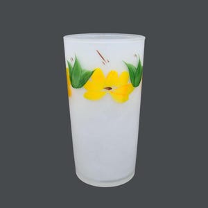 May include: White frosted glass drinking glass with yellow flowers and green leaves painted around the middle.