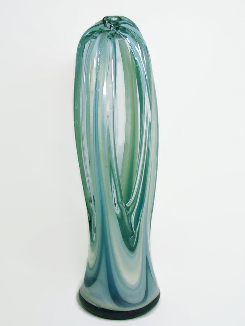 May include: A tall, slender glass vase featuring a swirling pattern of translucent teal, light blue, and white colors. The cylindrical body has a smooth, polished surface with vertical striations that taper slightly toward the rounded top opening.