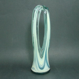 May include: A tall, clear glass vase featuring a swirling pattern of opaque white and translucent teal blue glass. The vase has a wide, circular base that tapers upward into two distinct, elongated vertical loops that meet at the top.