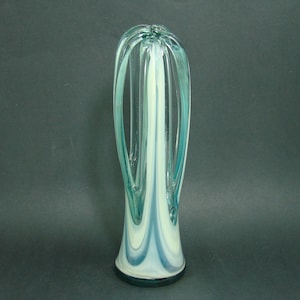 May include: A tall, slender glass vase featuring a swirling pattern of translucent teal and opaque white glass. The design includes elongated, arched glass loops that extend upward from the base, creating an open, airy structure with a smooth finish.
