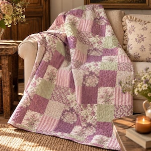 May include: A patchwork quilt featuring a repeating pattern of square fabric blocks in shades of lavender, sage green, and white. The design includes floral prints and vertical stripes with a quilted texture throughout the entire surface.